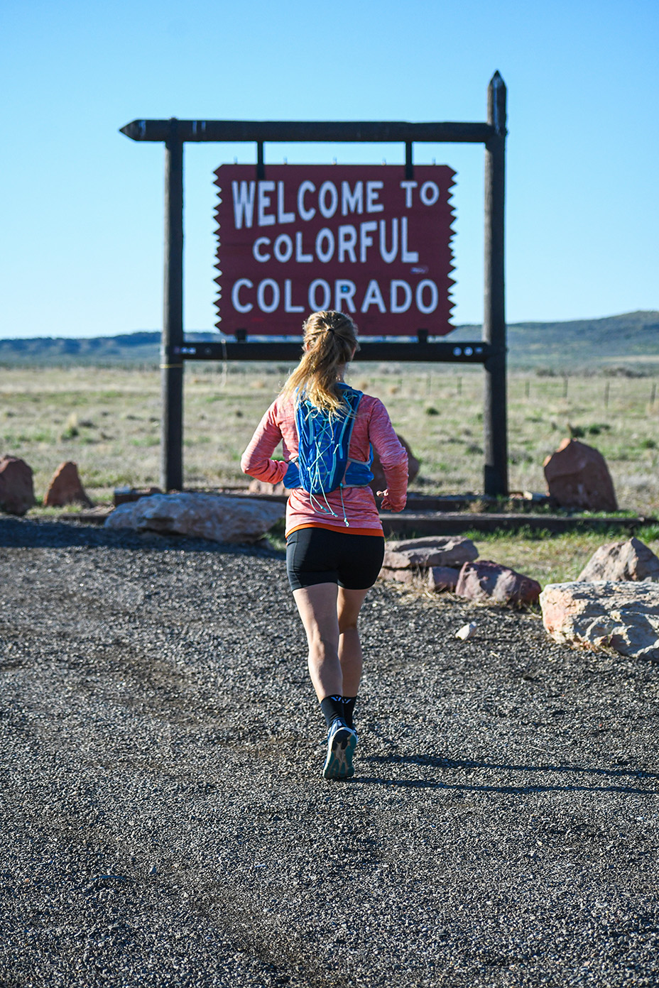 Meghan Guhler 鈥�16 running with back to the camera sign in front of her that says Welcome to Colorado